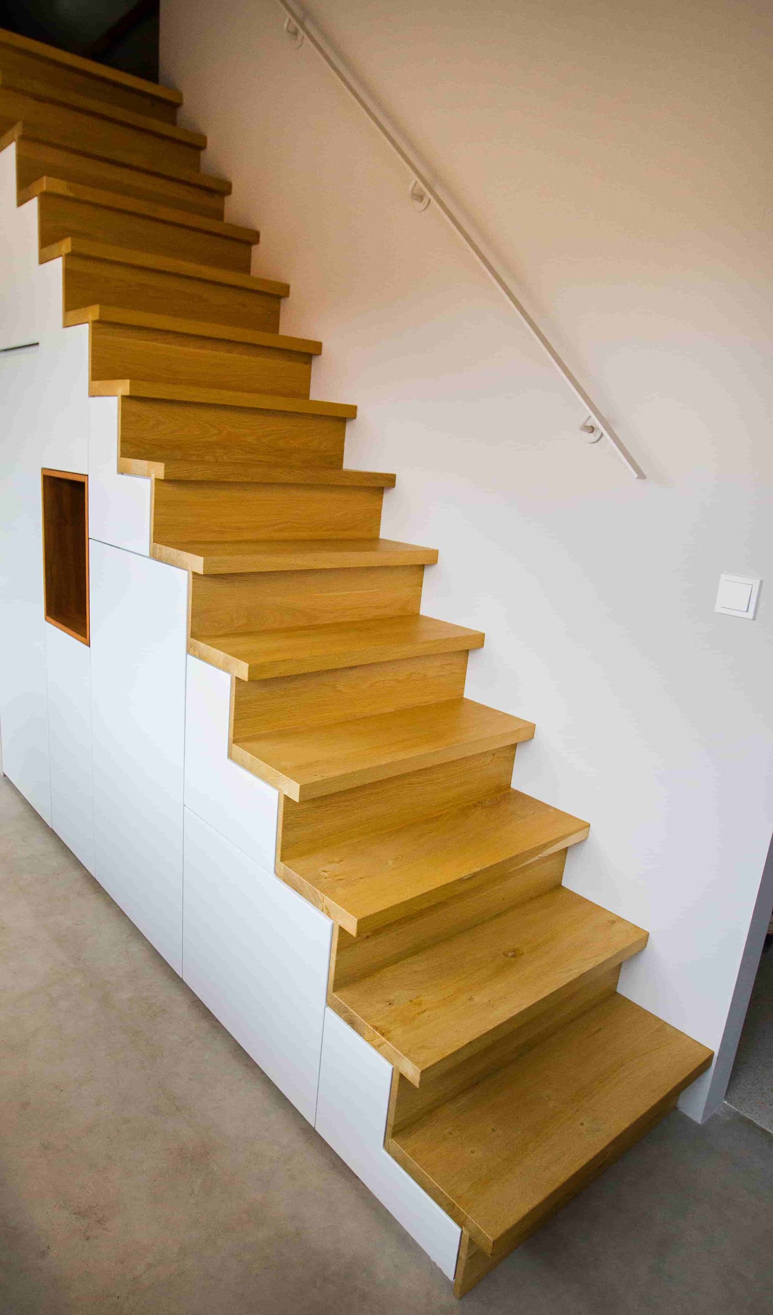 Trapkast op maat: witte kastenwand langs een houten trap