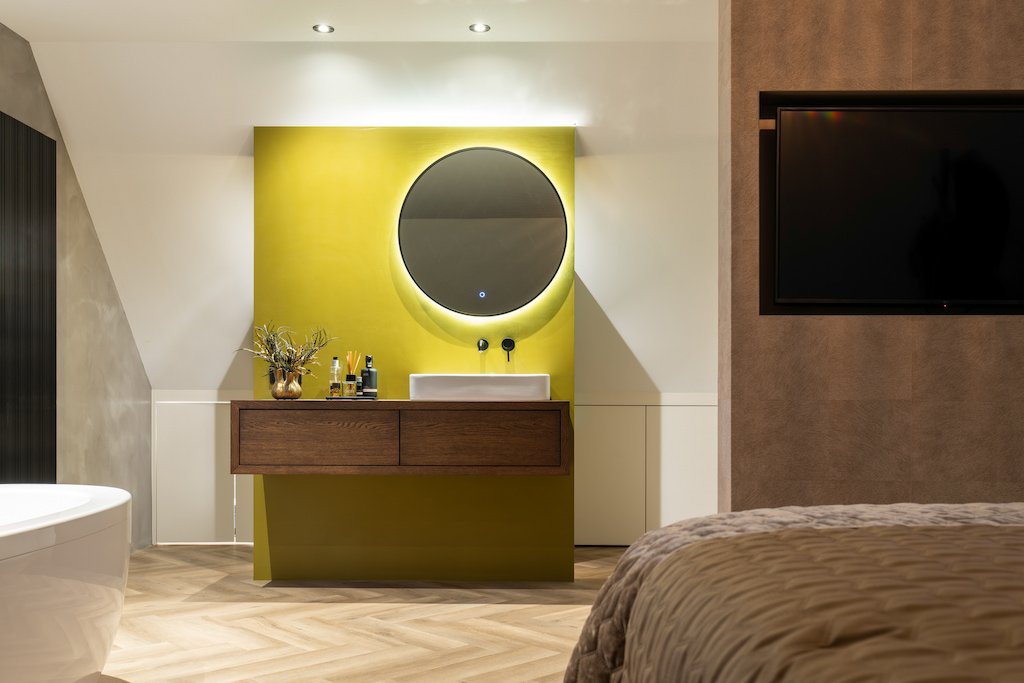 Badkamermeubel op maat met ronde spiegel voor gele wand in een slaapkamer met badkamer